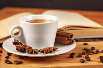 Coffee break with a Cup of hot strong coffee on a wooden table with an open old book covered with cloth. A white Cup of black coffee surrounded by a small amount of roasted coffee beans