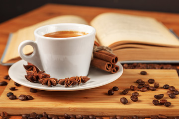 Coffee break with a Cup of hot strong coffee on a wooden table with an open old book covered with cloth. A white Cup of black coffee surrounded by a small amount of roasted coffee beans