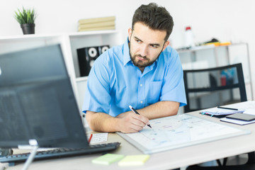 A young man standing in the office at a computer Desk and working with a magnetic Board.