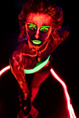 Portrait of a beautiful young sexy girl with ultraviolet paint on her body. Pretty woman with glowing bodyart in black lamp light
