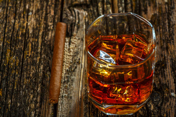Whiskey with ice in a glass on an old dark tree table. Whiskey or cognac on a wooden dark table. Whiskey. Selective focus.