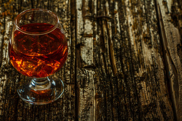 Whiskey with ice in a glass on an old dark tree table. Whiskey or cognac on a wooden dark table. Whiskey. Selective focus.