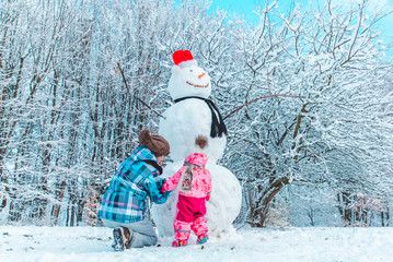 mother with daughter playing outside in winter time. making snowman