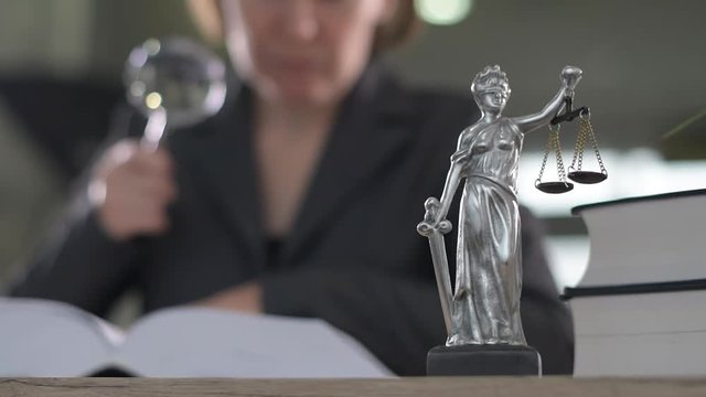 Attorney woman using magnifying glass for law book reading at her office desk, selective focus 