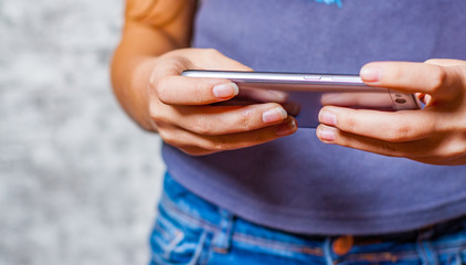 young teenager girl hand using mobile phone or smartphone on gray wall background