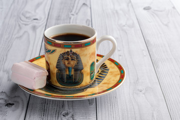 A Cup of coffee with Egyptian patterns and sweet marshmallows on a light wooden background