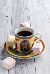 A Cup of coffee with Egyptian patterns and sweet marshmallows on a light wooden background