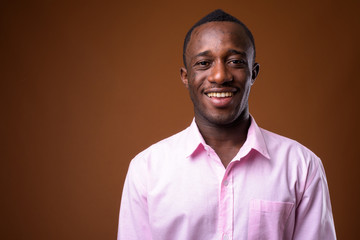 Portrait of young African businessman smiling against brown background