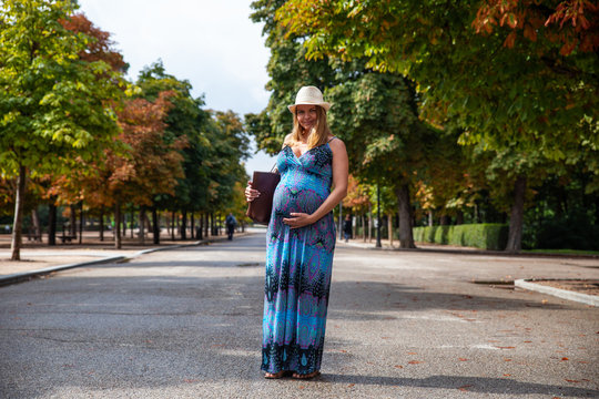Pregnant attractive woman with book in park