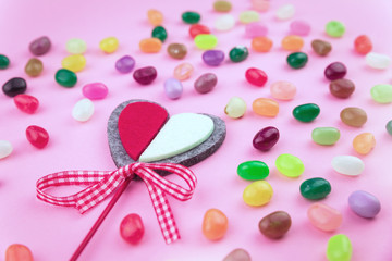 Jelly bean sweets and a festive crafted heart on pink background. Love and St Valentine's Day concept