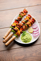 grilled chicken tikka on skewers.  served in a plate with green chutney and onion. Selective focus