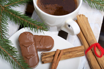 A cup of coffee, Cinnamon sticks and chocolate next to the fir branches. On a wooden box.