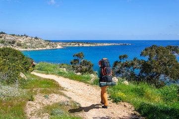 stylish girl in hat with backpack walking along the road among the flowers along the sea