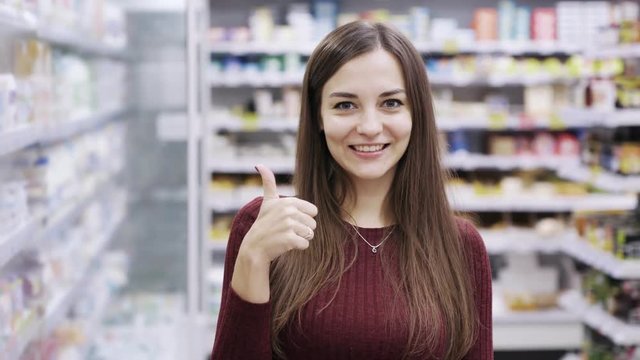Beautiful woman showing thumbs up sign in supermarket