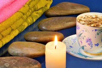 Fototapeta na wymiar Hot stone massage-stone therapy, for the treatment of many diseases. On a blue background stones for stone therapy, a bright candle, towels and coffee for tone.