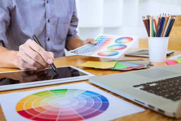 Young creative graphic designer working on project architectural drawing and color swatches, selection coloring on graphic chart with work tools and equipment