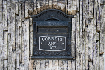 box of letters, mail box in iron in the dark gray color, on the stone wall. With drawing of a pigeon carrying a letter. With the word "Correio", letter in Portuguese.