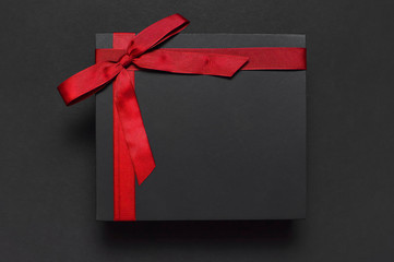 Black gift box with red ribbon on dark background top view flat lay. Holiday concept, birthday gift, father's day, Valentine's Day, new year or Christmas presents Xmas. Congratulations background