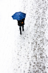 Woman under the umbrella on the snowy sidewalk