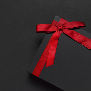 Black gift box with red ribbon on dark background top view flat lay. Holiday concept, birthday gift, father's day, Valentine's Day, new year or Christmas presents Xmas. Congratulations background