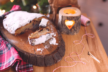 Traditional german christmas stollen on the rustic background with christmas decoration and fir tree. Traditional festive pastry, Christmas tree and garlands. Cozy holiday at home.