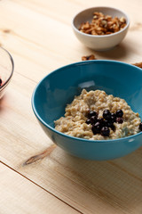 Porridge in a bowl with the berries, walnuts on bright wooden table. Healthy breakfast image. Copy space