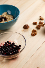 Porridge in a bowl with the berries, walnuts on bright wooden table. Healthy breakfast image. Copy space