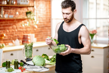 Portrait of a handsome sports man eating healthy vegetarian salad standing on the kitchen at home