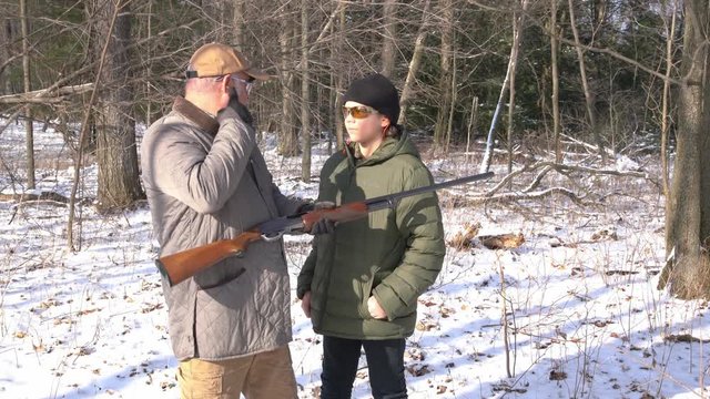 A father teaching his son how to shoot a shotgun safely in the woods in winter