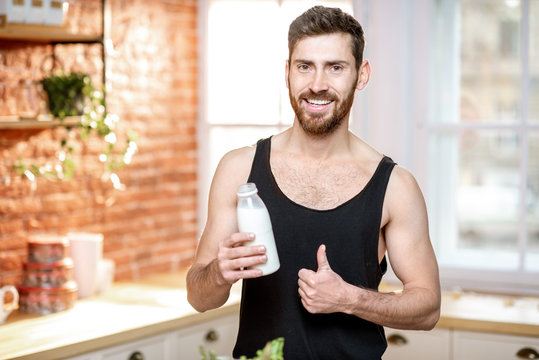 Portrait of a handsome sports man in black t-shirt drinking milk shake on the kitchen at home