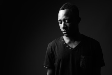 Fototapeta na wymiar Sad young African man against black background in black and white