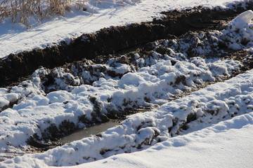 Snow-covered mud puddle with a track on a dirt road - winter countryside path