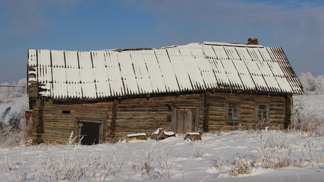 Abandoned wooden old barn with a snowy rickety roof - winter village landscape