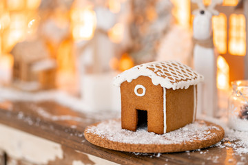 Christmas decorations and Holiday mood. Morning in the bright living room. Gingerbread house on wooden table. Defocused garland lights on background.