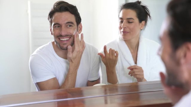 Attractive couple applying face and hand cream in bathroom