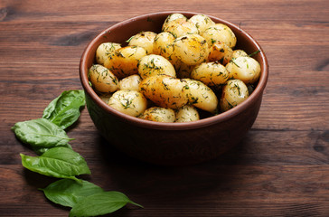 Freshly prepared potatoes with greens in a clay plate on a wooden board. Homemade organic food.