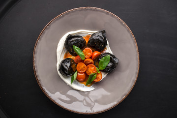 Traditional Italian black ravioli with cherry tomatoes on black background