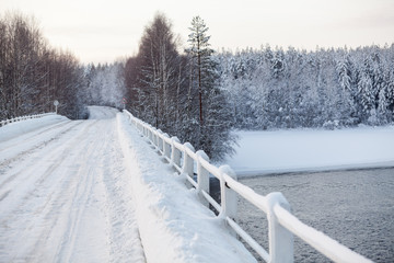 Snowy surface of empty country road on bridge across a river, winter season