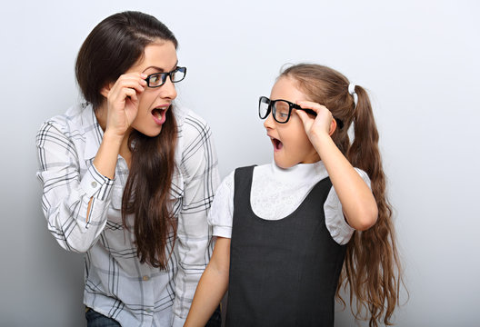 Happy surprising mother and excite kid in fashion glasses looking each other with opened mouth on empty copy space background.