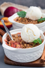 Plum crumble pie or plum crisp with oats and spices, served with vanilla ice cream ball, in baking dish, vertical