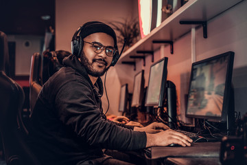 A young African American guy, enjoying spending time with his friends, playing in a multiplayer video game on a PC in a gaming club or internet cafe.