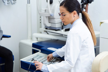Beautiful optician choosing lenses from set of corrective lens to her patient in ophthalmology...