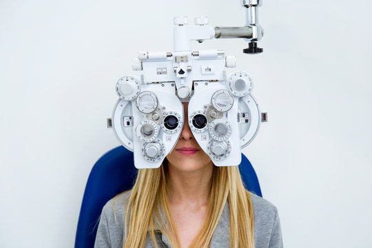 Pretty young woman doing eyesight measurement with optical phoropter in ophthalmology clinic.