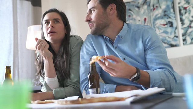 Relaxed couple in 30s sharing pizza at home with beer
