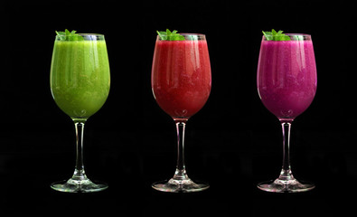 Green, pink and purple smoothies (soft drink) in glasses on a black background. Isolated objects