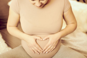 Pregnant woman making heart shape with hands on belly. 