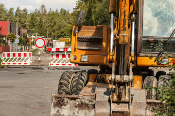 Detail on old yellow digger machine back, driver cabin visible, road closed signs, digged ground and removed asphalt, in background. Roadworks concept.
