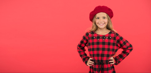 Wear beret like fashion girl. Kid little cute girl with long blonde hair posing in beret hat and checkered dress red background. Beret style inspiration. Fashionable beret accessory for female