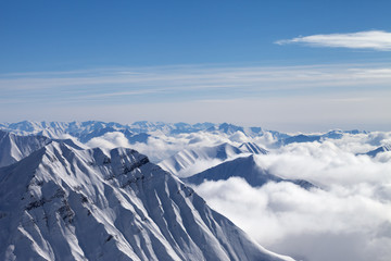 Snowy mountains in clouds and beautiful blue sky at nice winter day