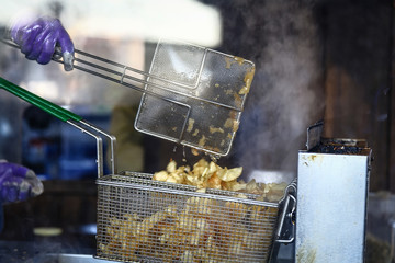 Chef pouring her newly fried potato chip in basket. Focus at the basket. The image shows moving colander.